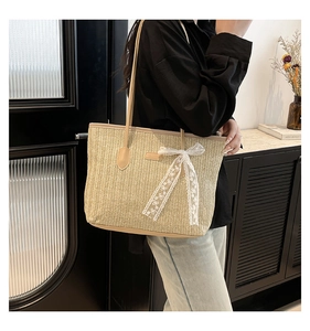 Detail of straw tote bag featuring white lace bow and elegant branded rectangle plaque
