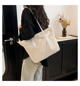 Détail du sac cabas en paille avec nœud en dentelle blanche et bordure en similicuir