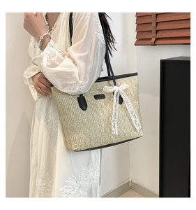 Detail of handwoven straw bucket bag featuring a white lace bow and black shoulder straps