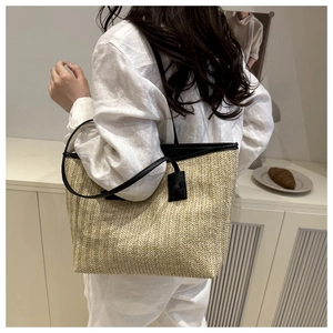 Straw tote bag with beige herringbone weave and black faux leather straps in detail