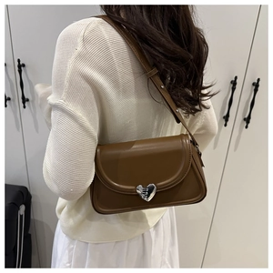 Detail of a brown leather shoulder bag featuring a textured silver heart lock clasp