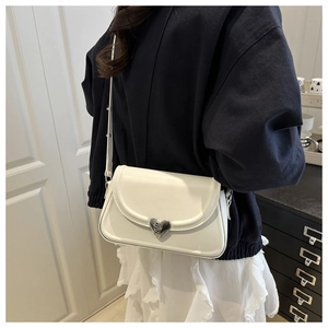Close-up of white leather crossbody bag with elegant silver heart-shaped metal buckle