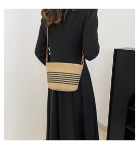 Detail of summer straw bucket bag with black stripes and brown shoulder strap on model