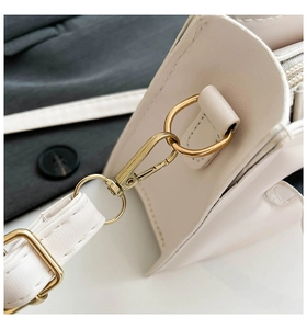 Nahaufnahme der goldenen Metallkarabiner und D-Ringe an einer beigefarbenen Ledertasche