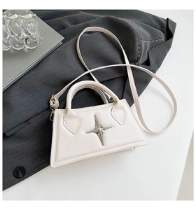Detail der cremefarbenen Trapez-Handtasche mit silbernem Stern auf grauem Blazer