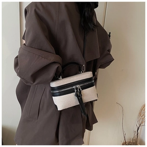 Détail d'un sac en toile beige avec finitions en cuir noir porté en bandoulière sur manteau