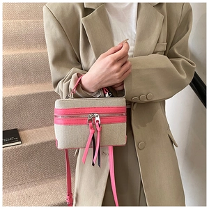 Detail of a beige canvas vanity box bag with pink leather trim held by a model