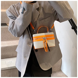 Detail view of small canvas box bag with bright orange leather trim and contrast straps