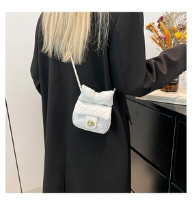 Detailed view of a white quilted mini crossbody bag with a bow on a black blazer