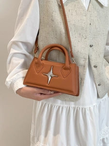 Braune Vintage-Handtasche mit silbernem Stern getragen mit weißem Hemd über der Schulter