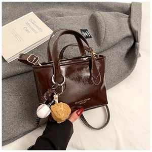 Macro view of polished dark brown oil wax leather bag with creative baseball charm detail