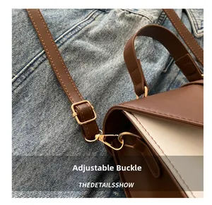 Detail of adjustable golden buckle and lobster clasp on dual-color leather shoulder bag