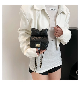 Detail shot of mini black crossbody bag featuring a large bow and gold rotary lock