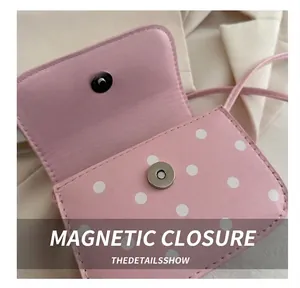 Detailed close-up of the magnetic metal closure on a pink polka dot leather crossbody bag
