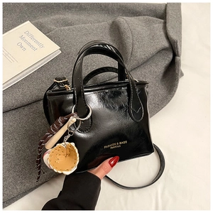 Detail of black patent leather mini tote bag with adjustable strap and glove charm