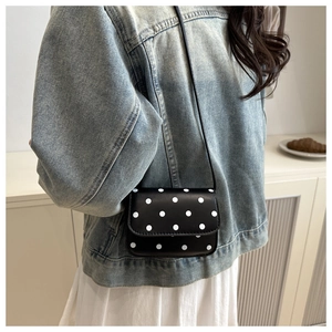 Close-up of polka dot crossbody bag worn with denim jacket in a cozy interior