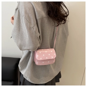 Detail of pink polka dot crossbody bag worn by model against a minimalist wall
