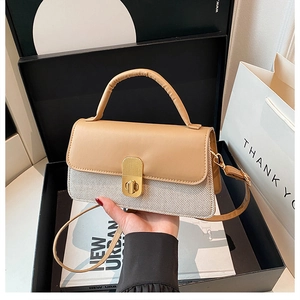 Detail der Kontrast-Handtasche mit goldenem Drehverschluss und Webtextur auf Geschenkbox