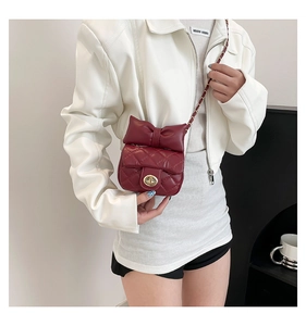 Detail of burgundy quilted mini crossbody bag with large bow and gold metal clasp