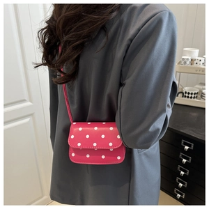Detailed side view of a pink polka dot mini crossbody bag on a grey blazer outfit