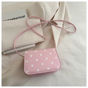 Detail of pink polka dot crossbody bag on beige blazer with a slim strap design
