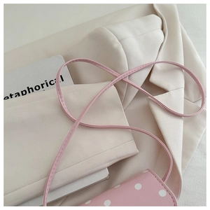 Detail of pink polka dot crossbody bag with leather strap and lifestyle background