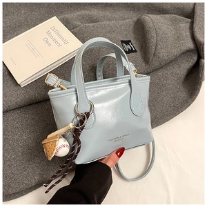 Detail of light blue glossy PU leather tote bag featuring a baseball glove charm