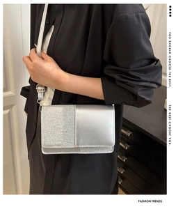 Detail of silver dual-texture rectangular crossbody bag shown on a model in black shirt