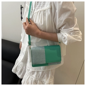Detail of green crossbody bag with glitter patchwork and adjustable strap on a white dress