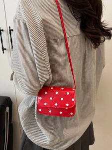 Red mini crossbody bag with white polka dots on a model wearing a striped shirt