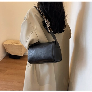 Détail d'un sac cylindrique en cuir noir avec une bandoulière tissée géométrique