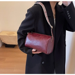 Detail of burgundy cylindrical bag with vintage texture and wide woven geometric strap