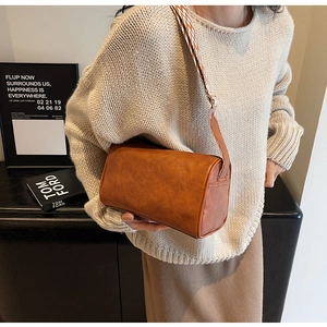 Detail of a brown cylindrical shoulder bag with an adjustable patterned woven strap