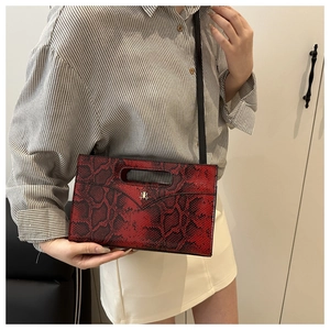 Detail einer Handtasche mit rotem Schlangenmuster, Metalllogo und schwarzem Riemen