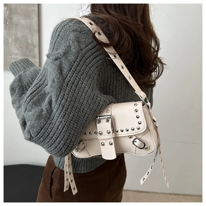 Détail du sac à bandoulière blanc cassé à rivets et boucles porté avec un pull en maille