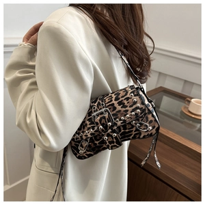 Détail d'un sac à bandoulière léopard avec clous argentés porté sur un blazer blanc