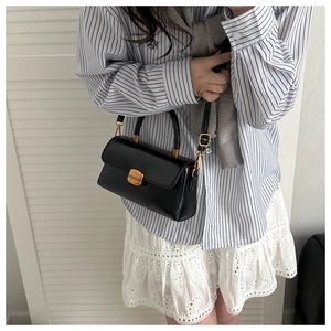 Detail of black crossbody bag with gold rectangular lock and adjustable shoulder strap