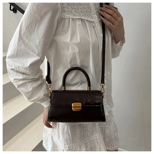 Detail view of a vintage dark brown leather handbag with a gold metal lock on a white dress