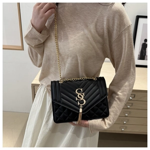 Model showing a black quilted shoulder bag with gold SS logo, tassel, and chain strap