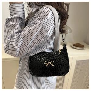 Detail of black patent leather baguette bag with textured circles and gold bow clasp
