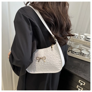 Détail du sac hobo blanc avec surpiqûres en cœur et nœud doré porté par le mannequin