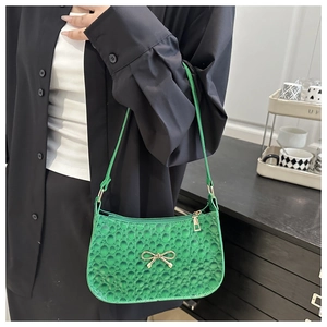 Close-up of green embossed shoulder bag featuring a gold bow metallic buckle