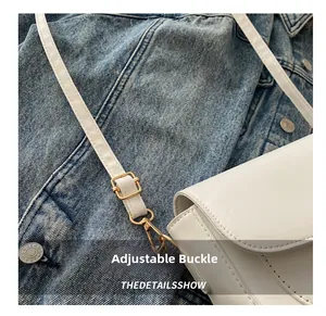 Détail de la boucle métallique dorée réglable sur un sac de selle blanc en similicuir