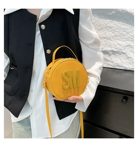 Close-up of circular yellow leather crossbody bag with 3D embossed letters and handle