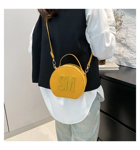 Detail of a yellow semi-circular crossbody bag with metal SM lettering and adjustable strap