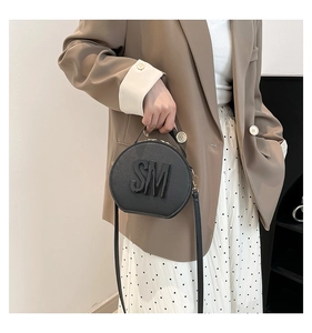 Close-up of a black circular crossbody bag featuring embossed SM lettering on a model