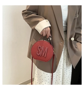 Detail of round red crossbody bag with bold SM embossed letter and matte leather finish