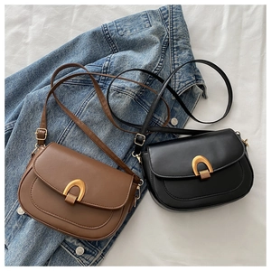 Sacs bandoulière noir et marron avec boucles dorées sur un lit blanc et jean bleu