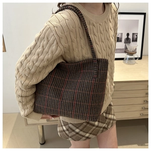 Detail of checkered tote bag with brown and red pattern shown on model's shoulder