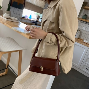 Sac sous le bras élégant en cuir rouge vin avec boucle dorée sur un trench beige